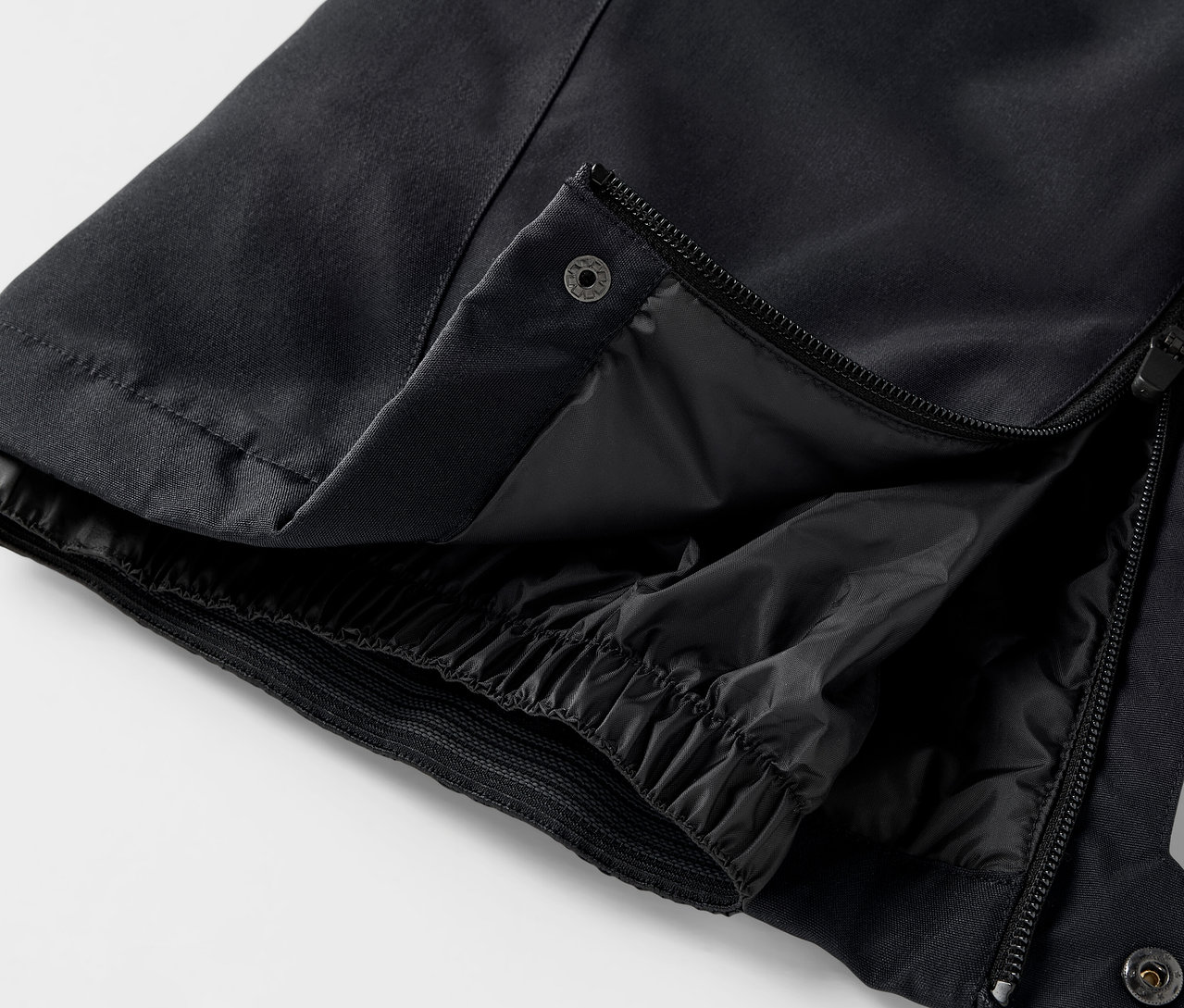 Detail einer schwarzen Hose mit geöffnetem Reißverschluss und Druckknopf.
