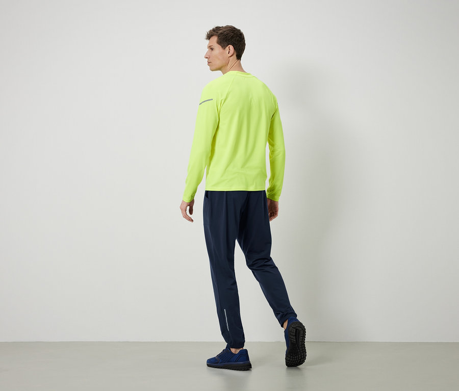 Mann in neon gelbem Langarmshirt und dunkelblauen Trainingshosen.