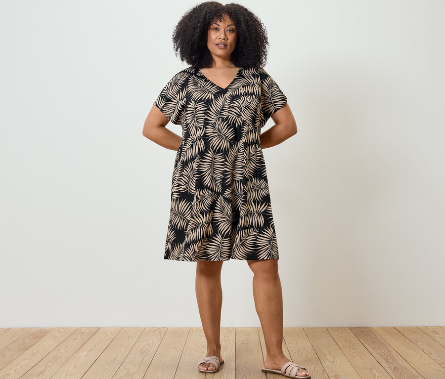 Eine Frau steht mit den Händen hinter dem Rücken und trägt ein bedrucktes Jerseykleid.