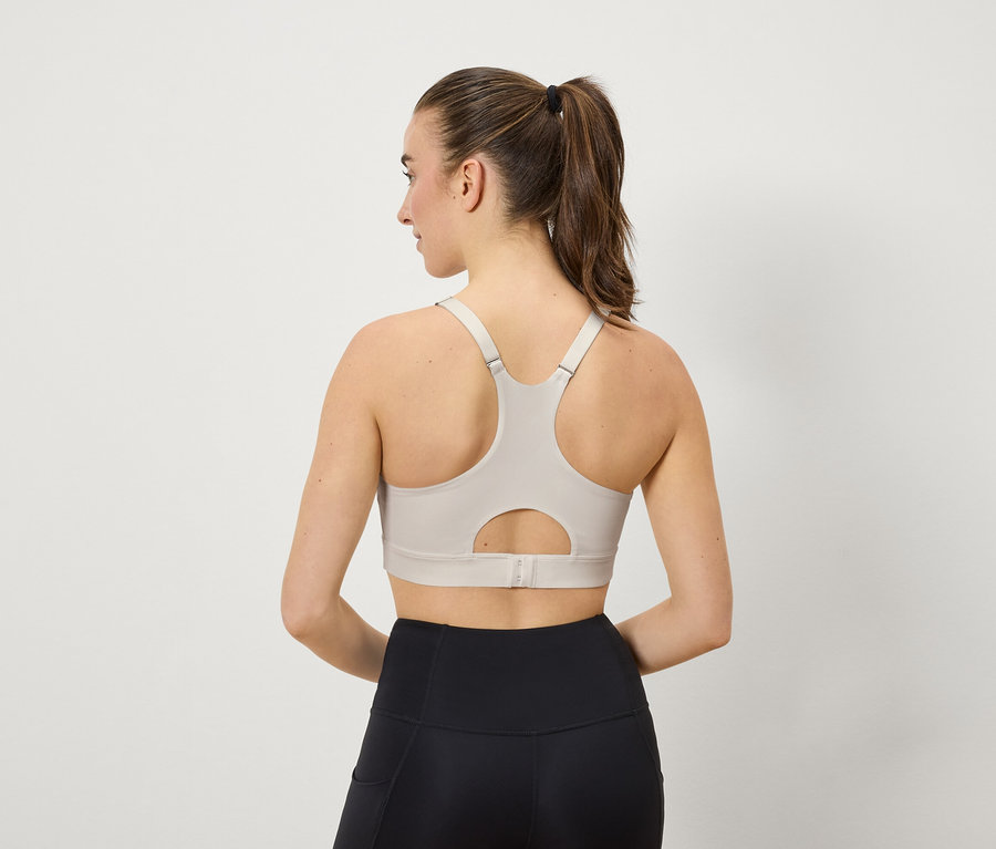 Frau von hinten, trägt einen beigen Sport-BH und schwarze Leggings.