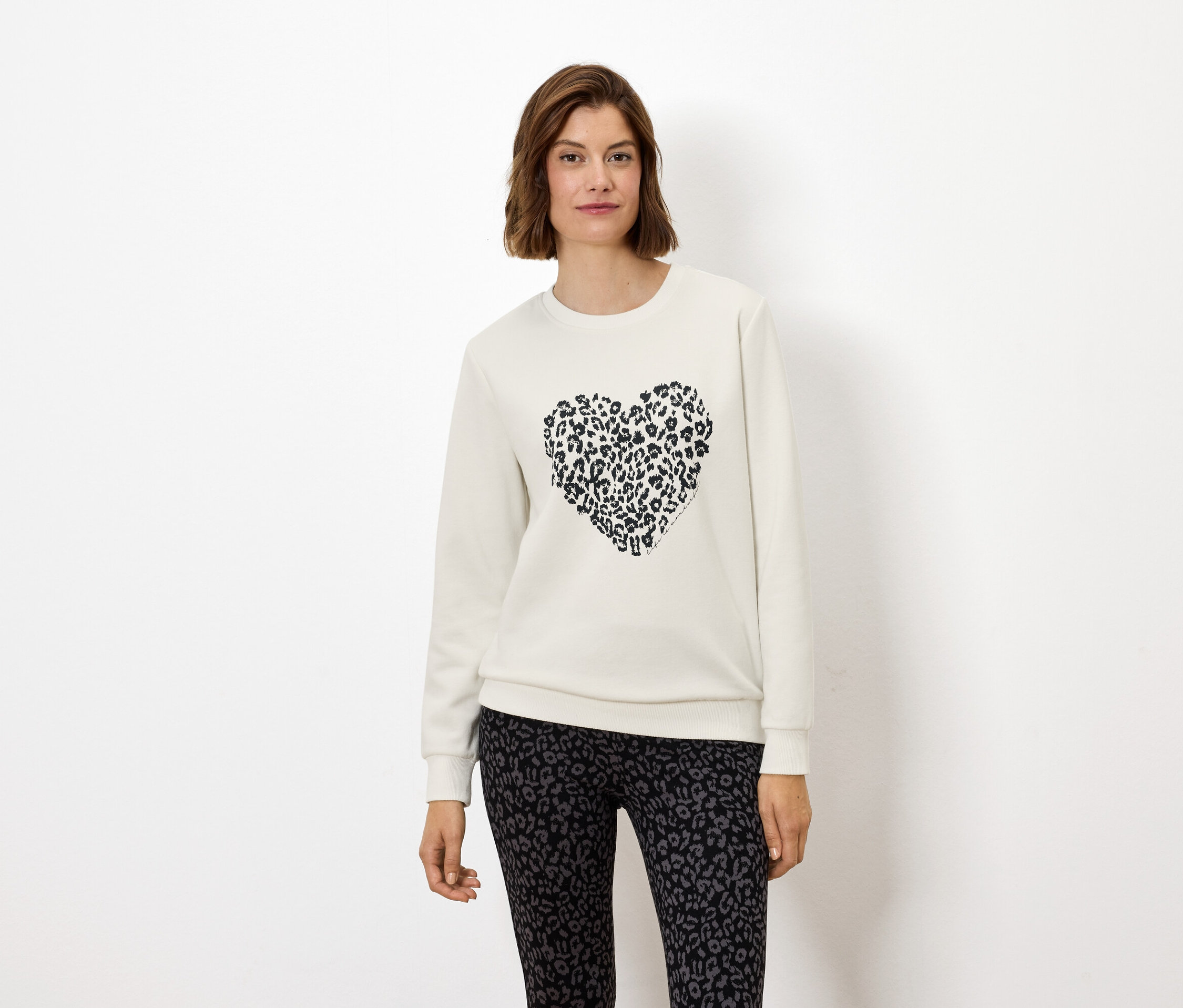 Frau trägt ein weißes Sweatshirt mit einem Tierdruckherz und Leggings mit Tierdruck.