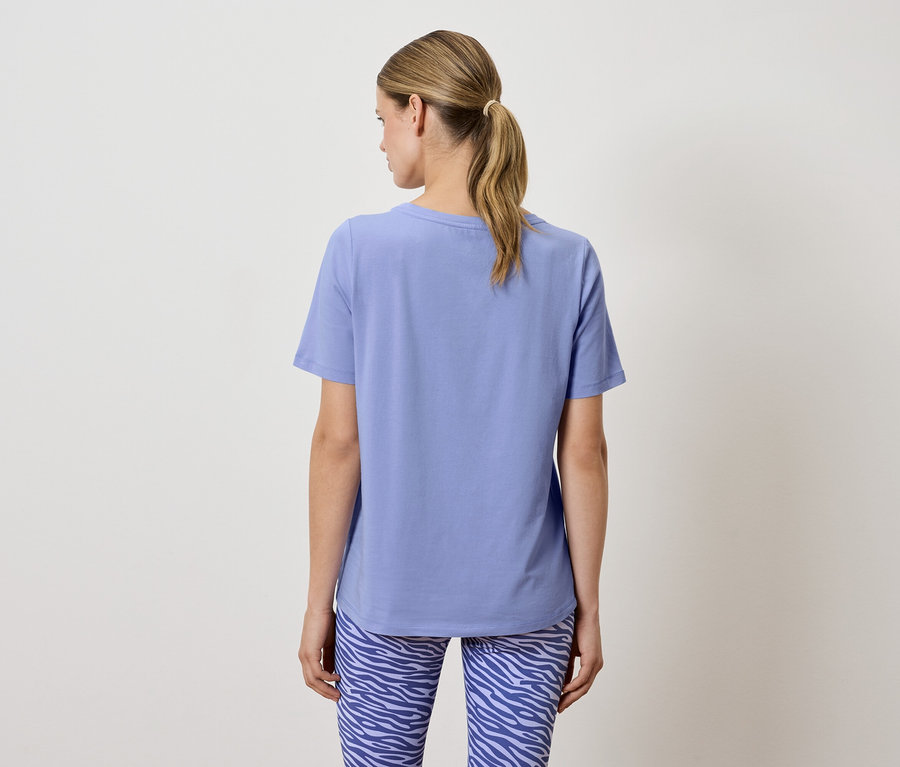 Frau mit dem Rücken zur Kamera trägt ein blaues T-Shirt und Leggings mit Tiermuster.