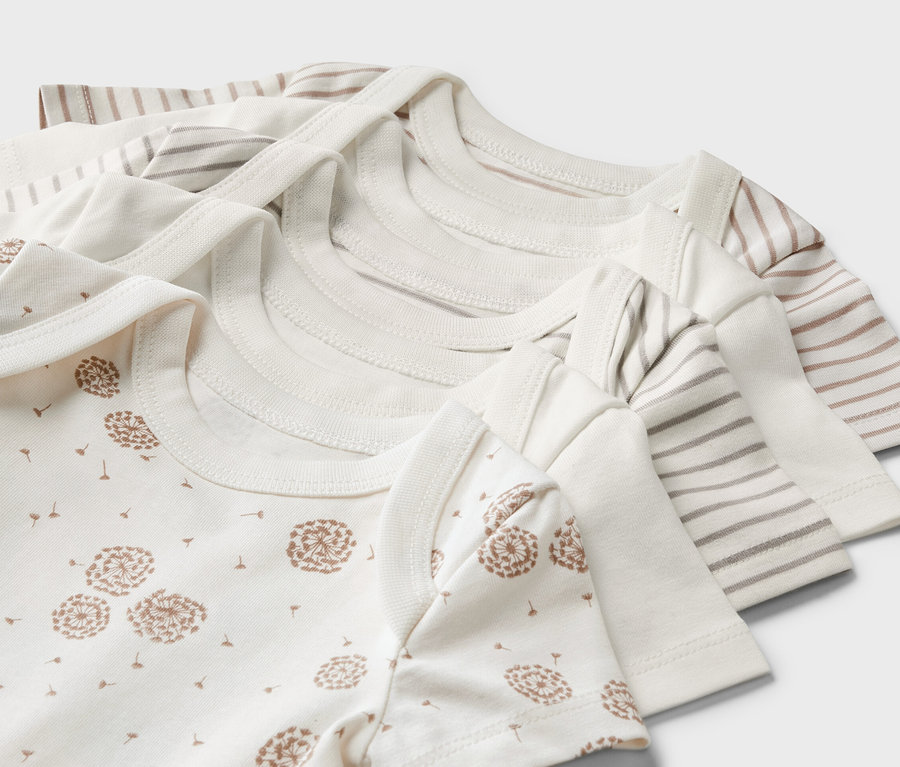 Nahaufnahme von fünf Baby-Bodys mit kurzen Ärmeln, darunter ein Body mit Löwenzahn-Print und andere mit Streifen.