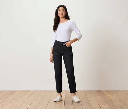 Frau posiert in schwarzen Jeans, weißem Dreiviertelarm-Top und weißen Turnschuhen.