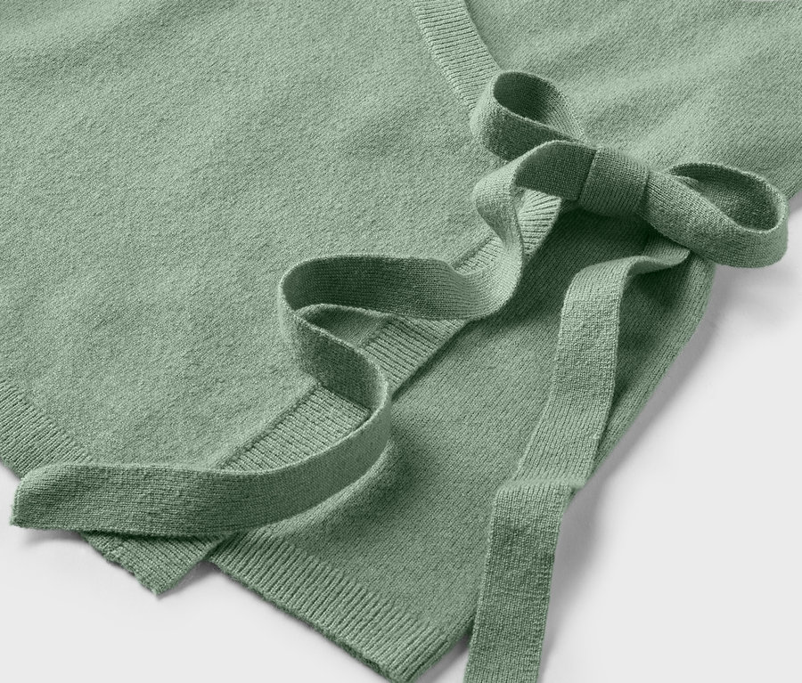 Detailaufnahme eines hellgrünen Wickelpullovers mit Bindeband.
