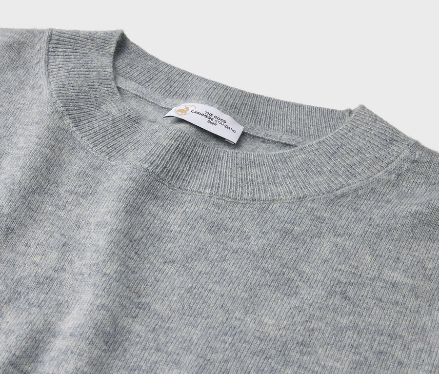 Detailaufnahme eines grauen Kaschmirpullovers mit Rundhalsausschnitt und Etikett.