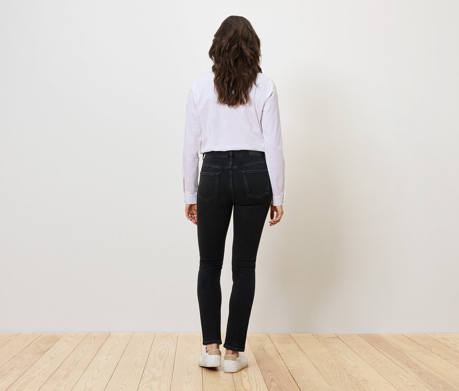 Frau von hinten trägt schwarze Jeans, ein weißes Hemd und weiße Turnschuhe.