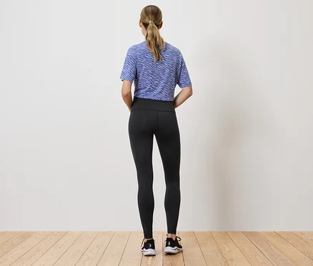 Eine Frau mit schwarzen Leggings und einem blau-weißen Oberteil steht mit dem Rücken zur Kamera.