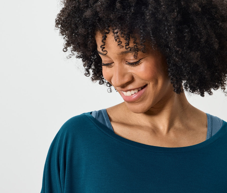Lächelnde Frau mit Afro trägt ein blaugrünes Oberteil.