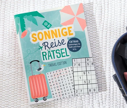 Buch »Sonnige Reise Rätsel« liegt neben einem offenen Koffer.