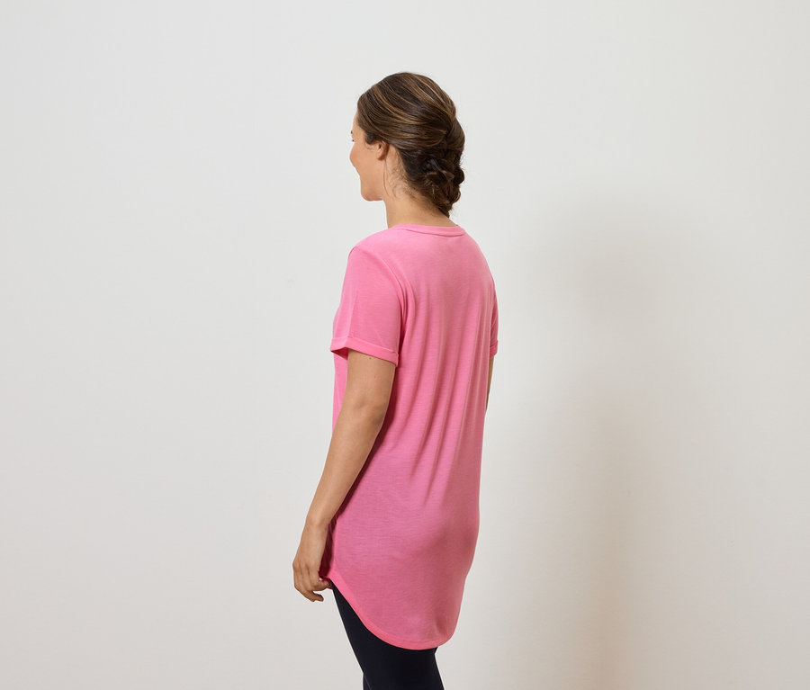Frau mit dem Rücken zur Kamera trägt ein pinkes T-Shirt und eine dunkle Hose.