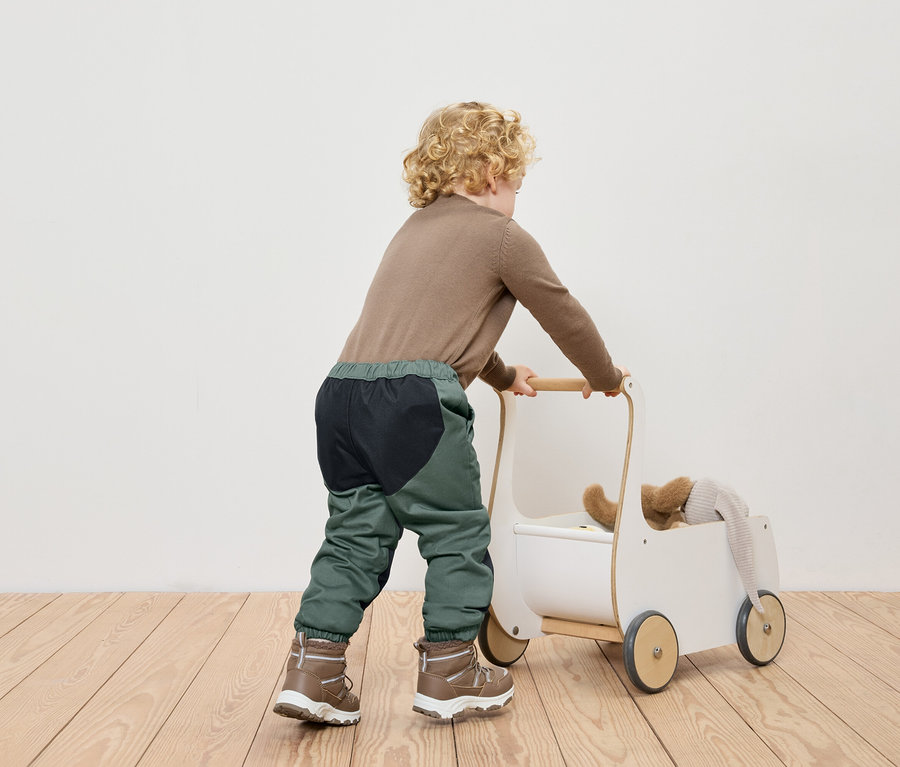 Ein Junge schiebt einen weißen Spielzeugwagen auf einem Holzboden.