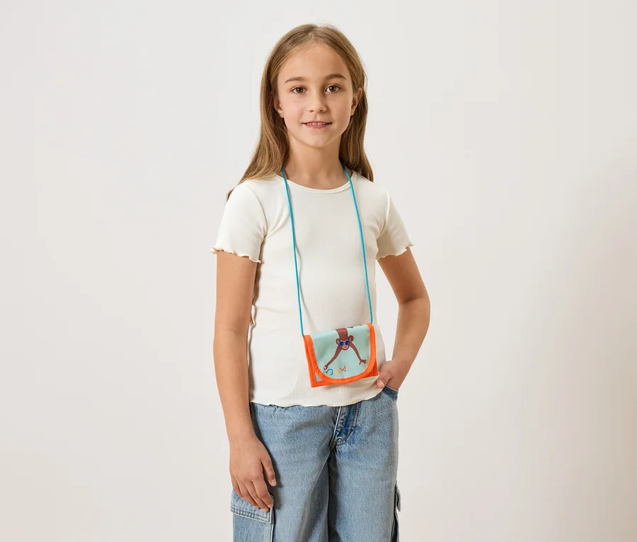 Mädchen mit hellem T-Shirt und Jeans, trägt eine kleine Umhängetasche mit einem Affen darauf.