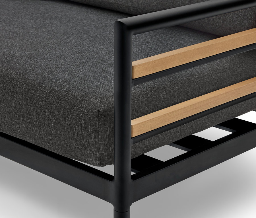 Nahaufnahme eines Sessels mit einem grauen Kissen, einem schwarzen Rahmen und Holzdetails.