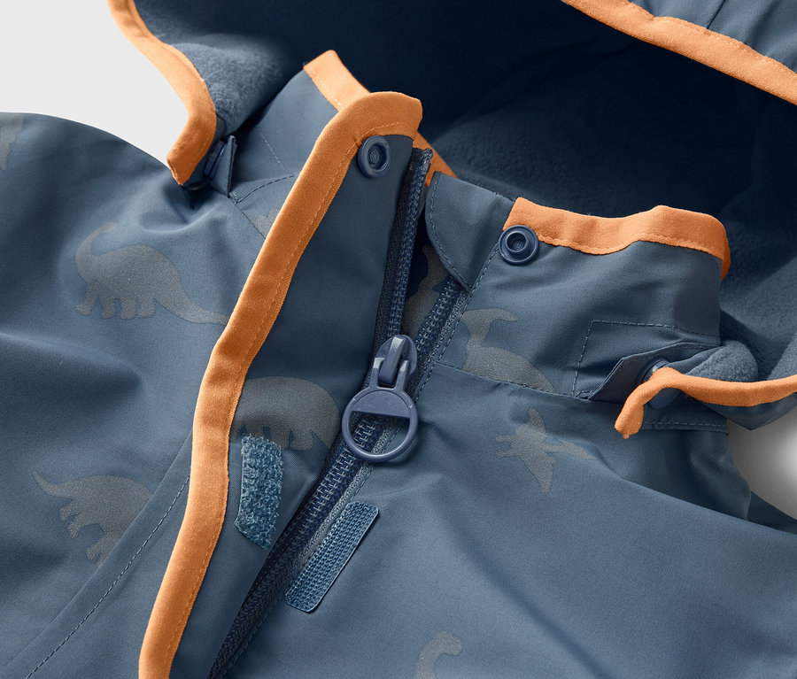 Nahaufnahme einer blauen Jacke mit Dinosaurier-Muster, orangefarbenen Akzenten und Reißverschluss.