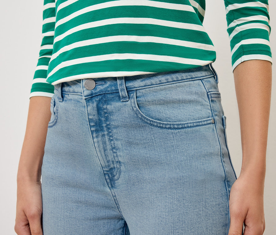 Nahaufnahme einer Person, die hellblaue Jeans und ein grün-weiß gestreiftes Oberteil trägt.