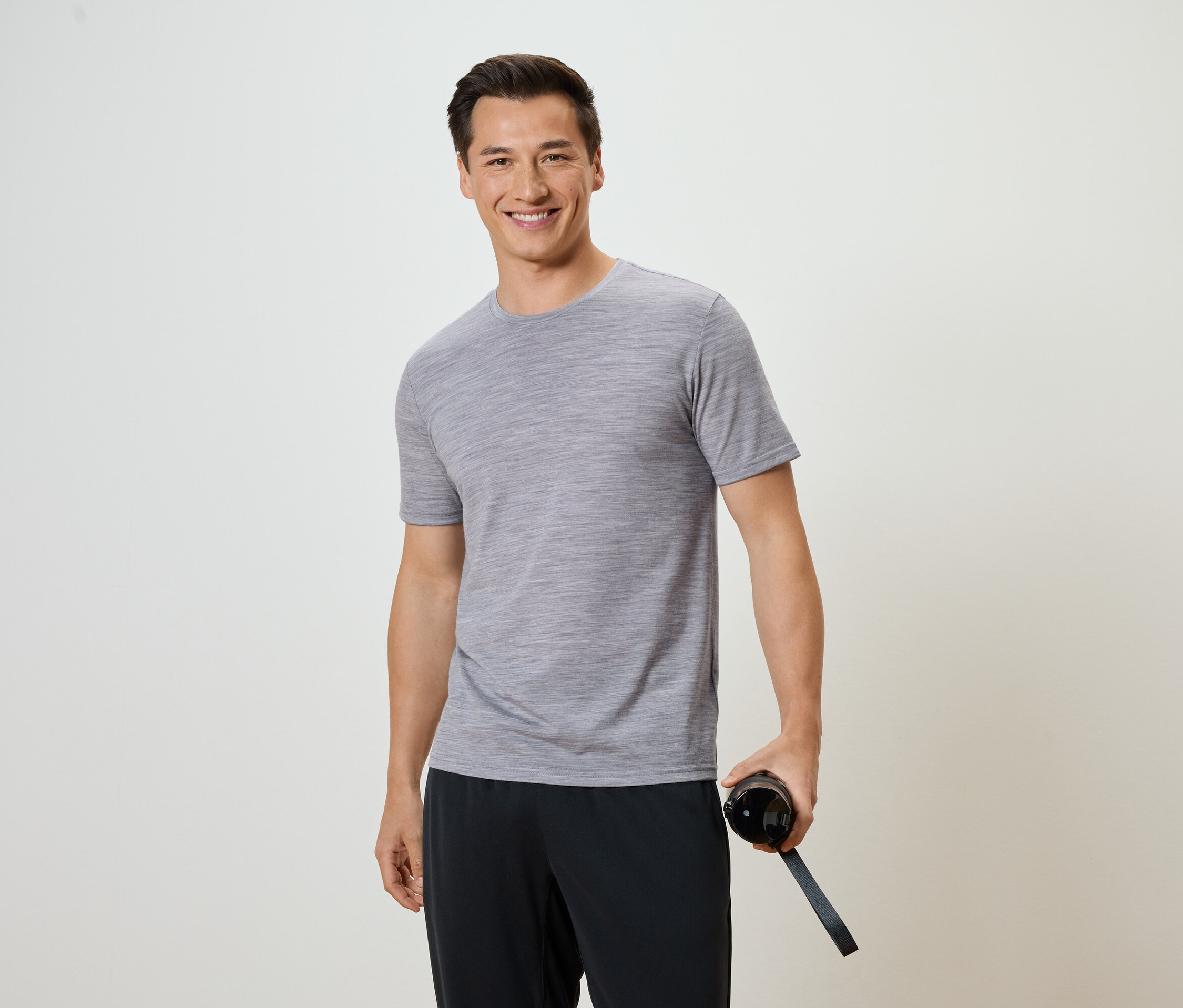 Mann mit grauem T-Shirt und schwarzer Hose hält eine Wasserflasche.