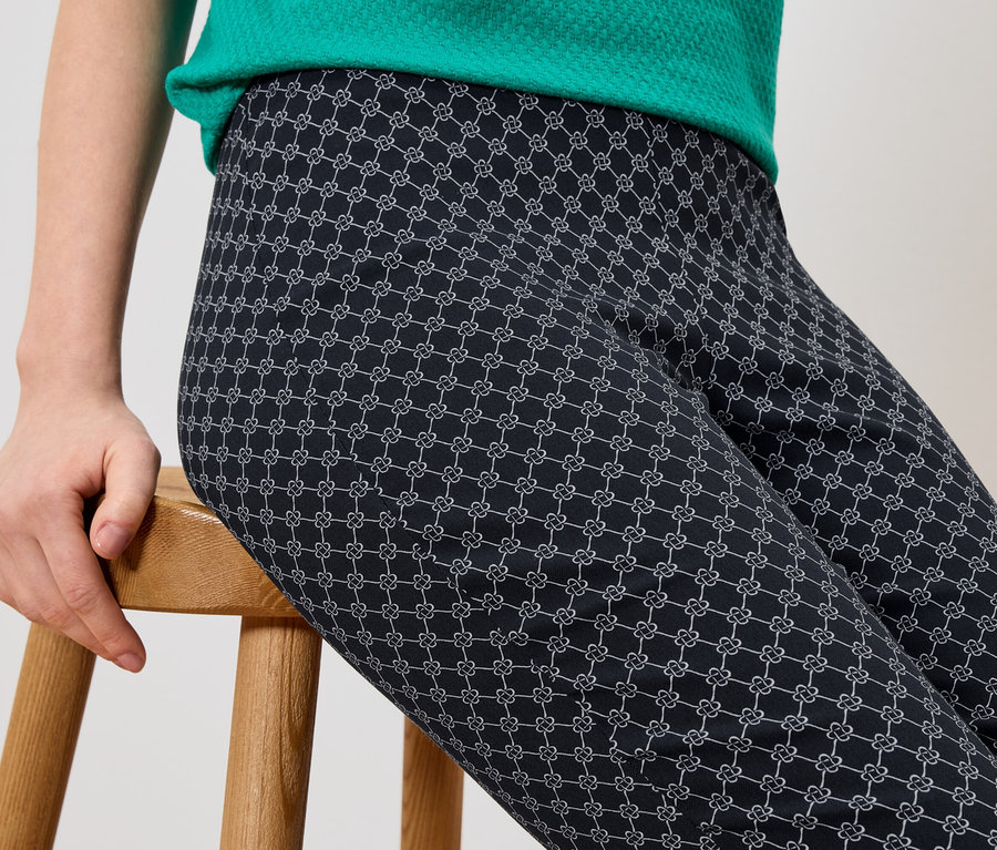 Person sitzt auf einem Holzschemel und trägt eine Hose mit einem grafischen Muster.