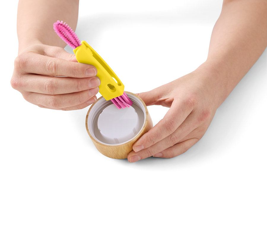 Eine Person reinigt einen Bambusbecher mit einer gelben Reinigungsbürste mit pinken Borsten.