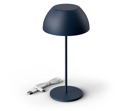 Eine dunkelblaue Lampe steht auf einem weißen Untergrund. Das Kabel der Lampe liegt daneben.