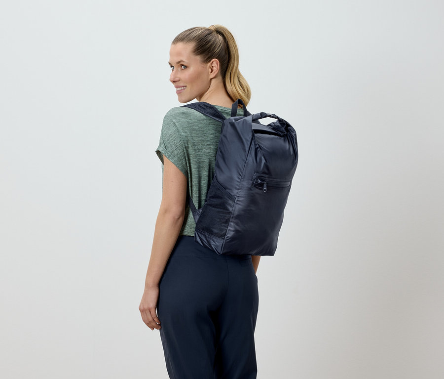 Frau mit blonden Haaren, von hinten gesehen, trägt einen marineblauen Rucksack.