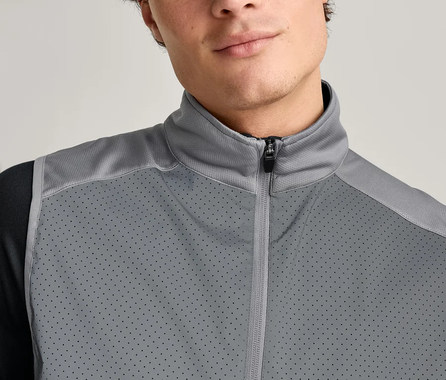 Nahaufnahme eines Mannes mit einer grauen, ärmellosen Jacke mit Reißverschluss über einem schwarzen Langarmshirt.