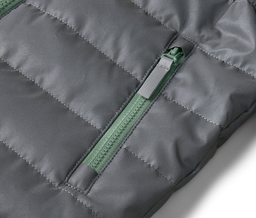 Nahaufnahme einer grauen Steppjacke mit einem grünen Reißverschluss an der Tasche.