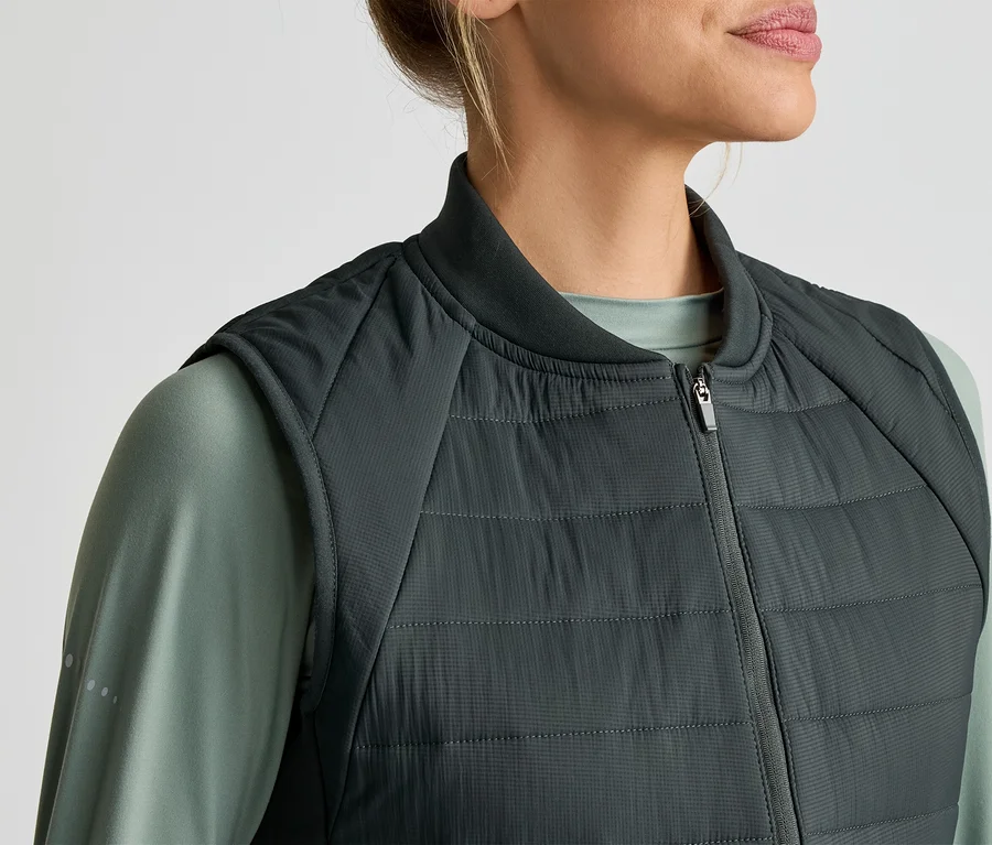 Frau mit grauem, gestepptem Bodywarmer über einem grünen Langarmshirt.