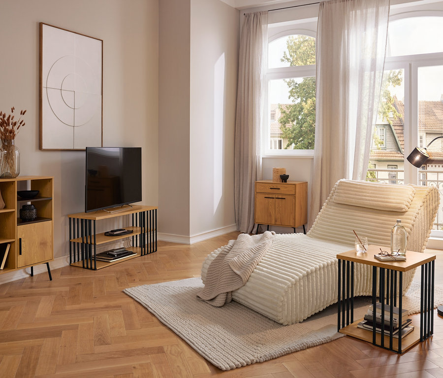 Modernes Wohnzimmer mit einer cremefarbenen Récamiere auf einem hellen Teppich, einem Holzschrank, einem TV-Möbel und einem Beistelltisch. Große Fenster mit Vorhängen blicken nach draußen.