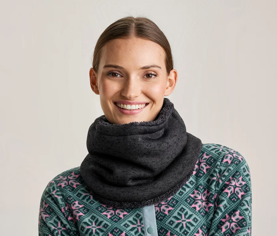 Lächelnde Frau mit einem dunkelgrauen Halswärmer und einem grün-rosa gemusterten Fleece-Oberteil.