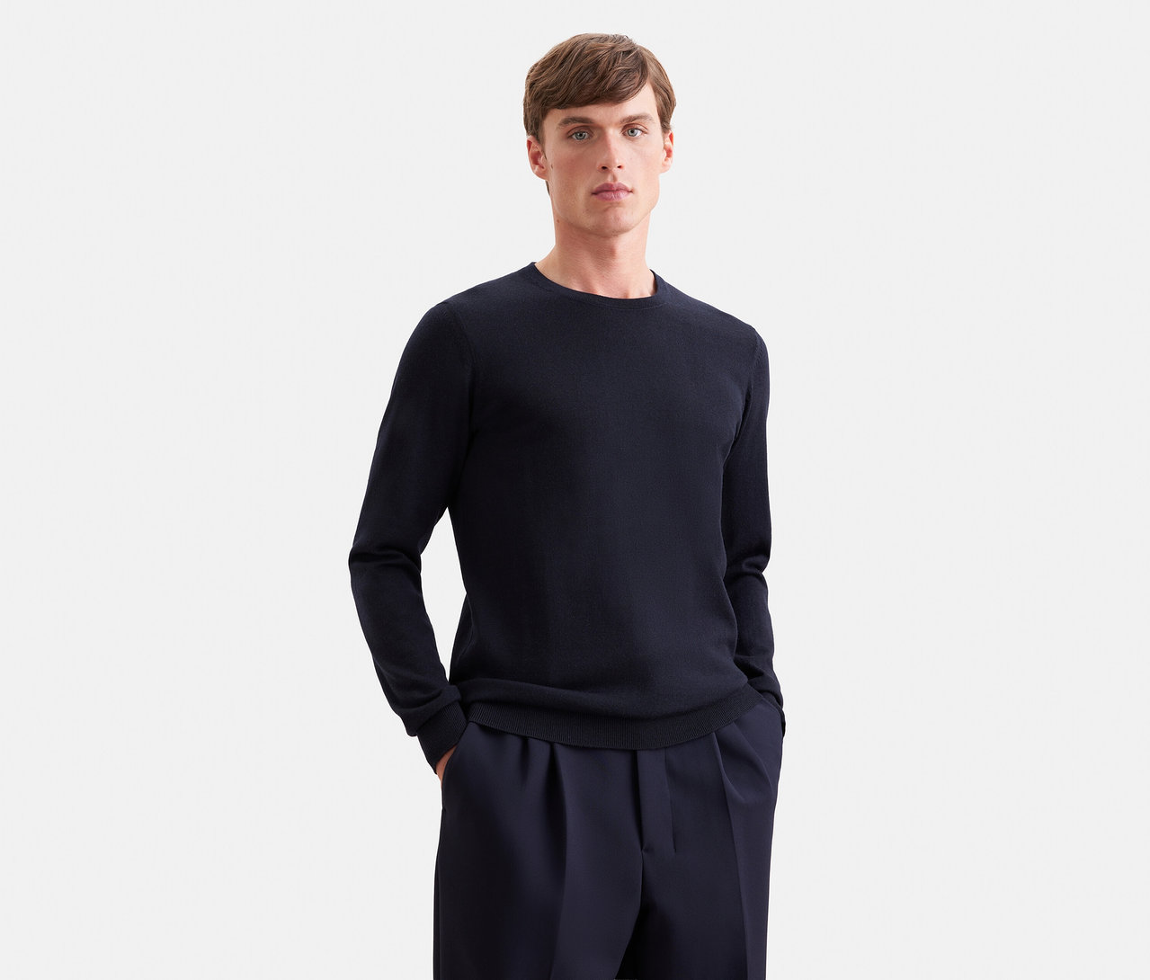 Mann in dunkelblauem Langarmpullover und dunkelblauer Hose, Hände in den Hosentaschen.