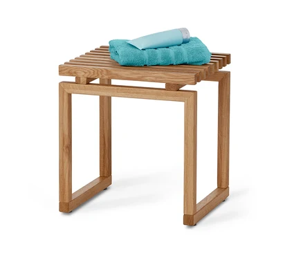 Auf einem Holzhocker liegen ein türkises Handtuch und eine hellblaue Tube.