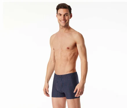 Lächelnder Mann, oberkörperfrei, trägt dunkelblaue SCHIESSER Shorts mit roten und weißen Streifen.