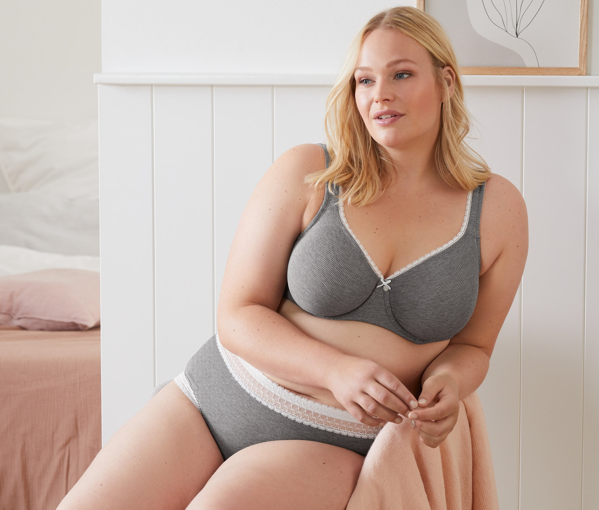 Frau sitzt und trägt einen grauen Bügel-BH und graue Slips.
