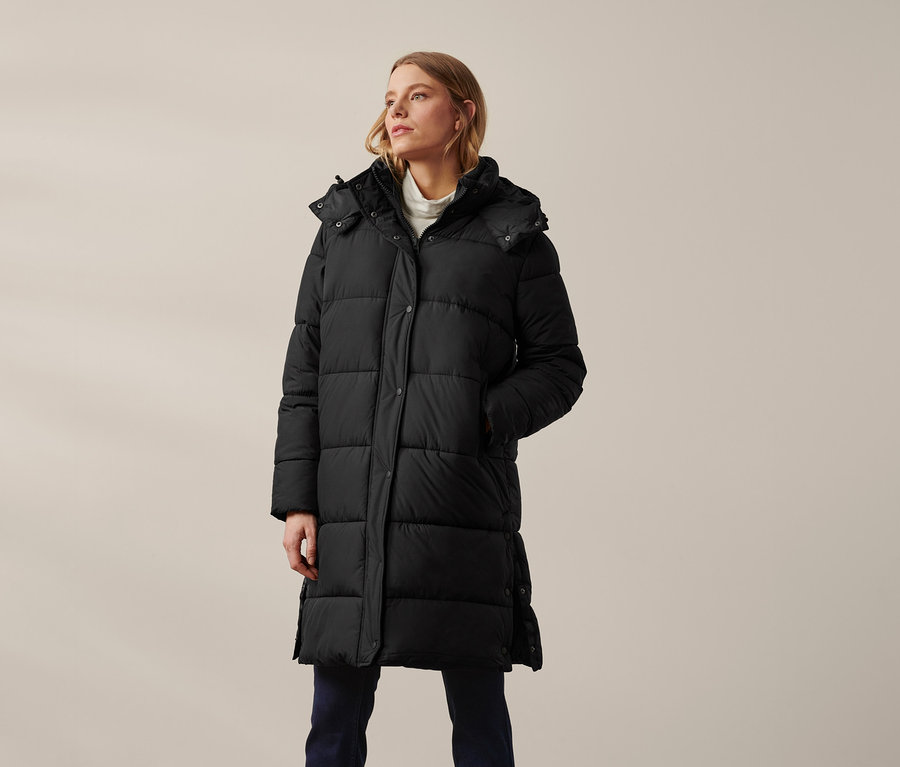 Frau trägt einen schwarzen Steppmantel mit Kapuze.