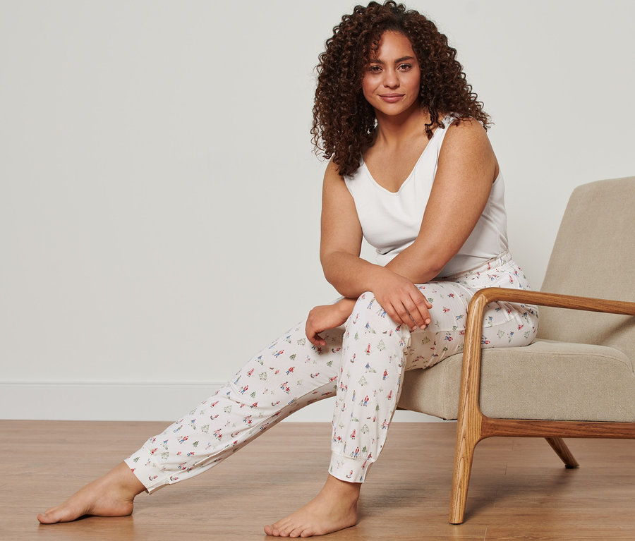 Frau sitzt im Sessel und trägt ein weißes Hemdchen (2 Hemdchen) und eine Jersey-Relaxhose.