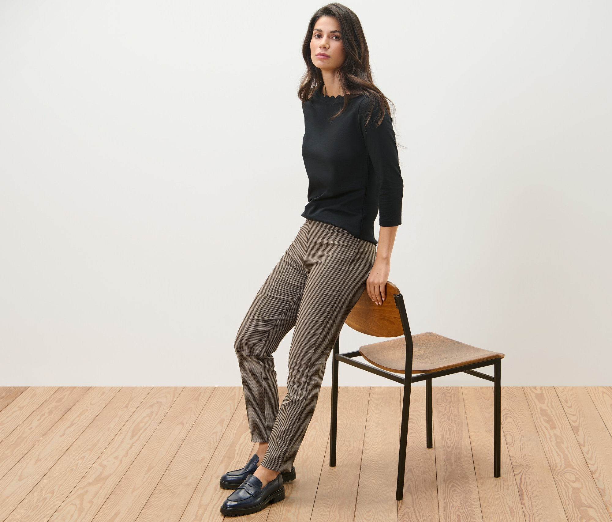 Frau sitzt seitlich auf einem Stuhl, trägt ein schwarzes Oberteil und eine Stretchhose mit Hahnentritt-Jacquard.