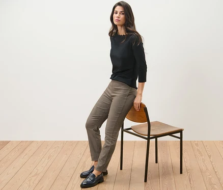 Frau sitzt seitlich auf einem Stuhl, trägt ein schwarzes Oberteil und eine Stretchhose mit Hahnentritt-Jacquard.