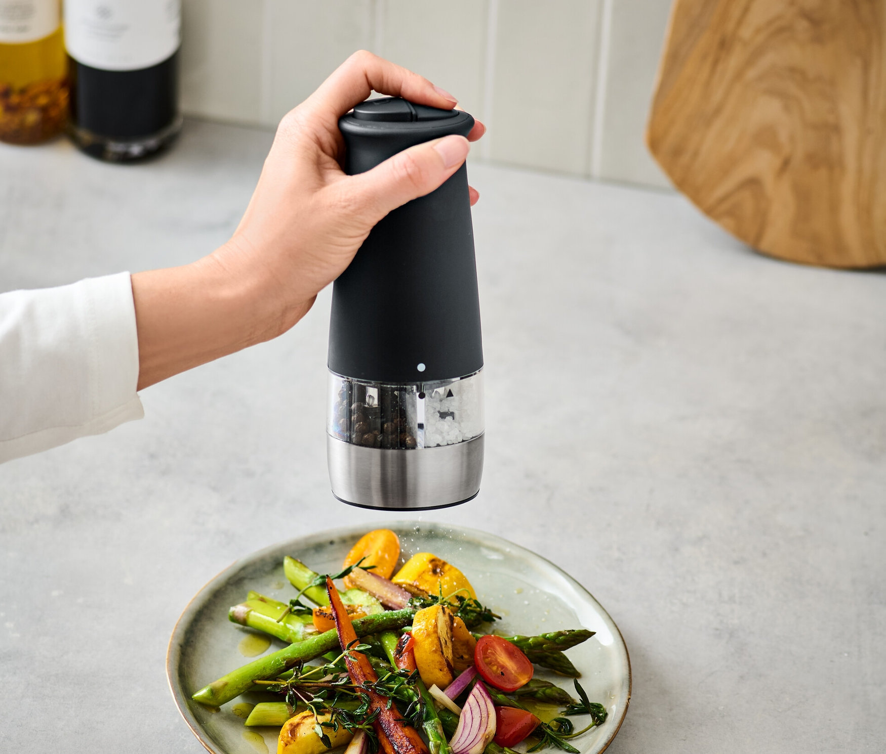 Eine Hand benutzt eine elektrische 2-in-1-Salz-und-Pfeffermühle über einem Teller Gemüse.