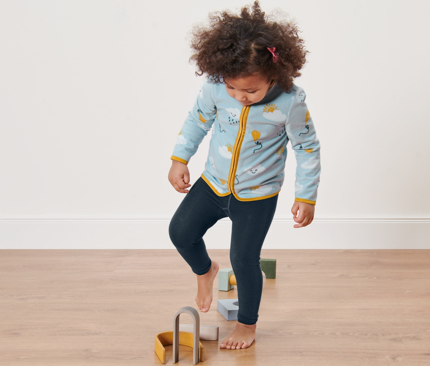 Mädchen steigt auf Holzspielzeug am Boden. Sie trägt 2 Kinder-Strickleggings.