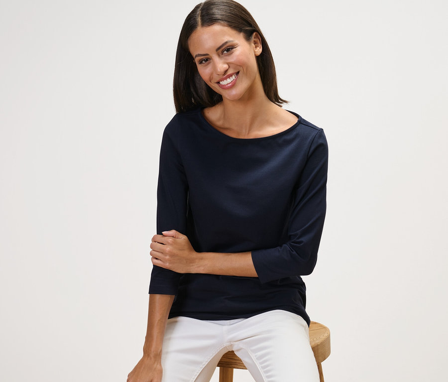 Frau sitzt auf einem Hocker und trägt ein marineblaues Shirt mit 3/4-Arm.