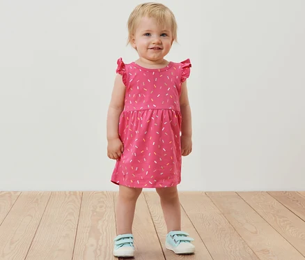 Lächelndes kleines Mädchen steht und trägt ein rosafarbenes Jerseykleid.