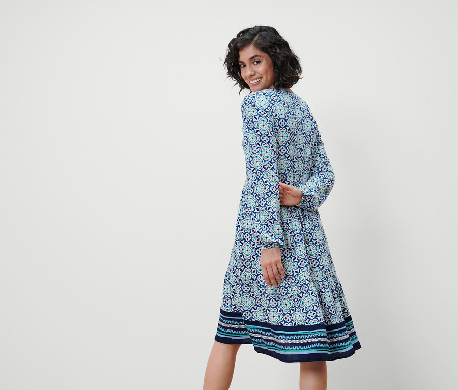 Frau blickt über die Schulter und trägt ein Webkleid mit Alloverprint.