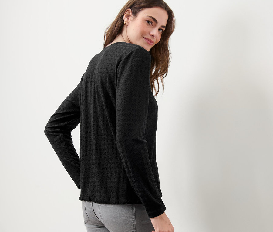 Eine Frau blickt über ihre Schulter und trägt ein strukturiertes, schwarzes Langarmshirt.