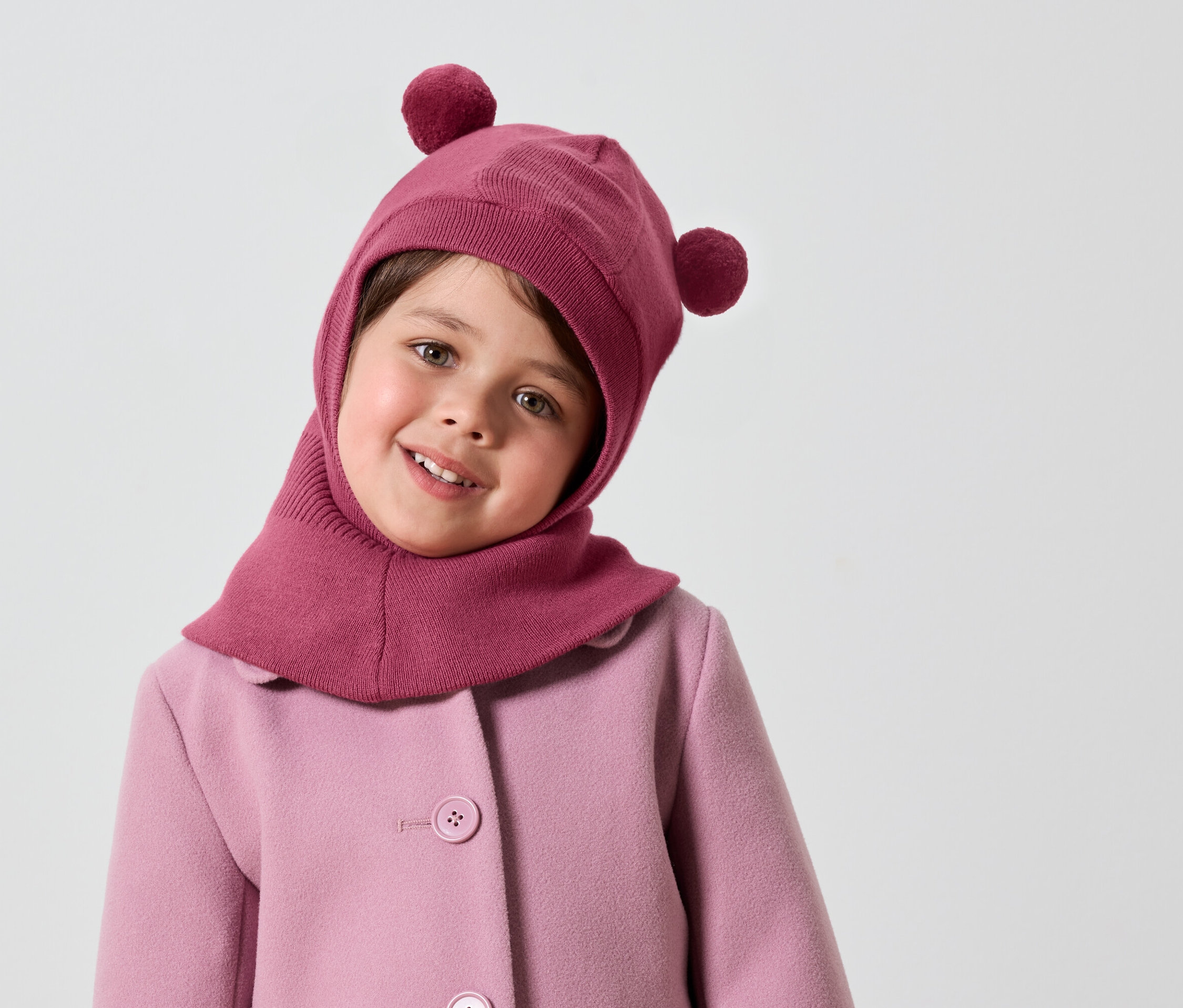 Lächelndes Mädchen mit rosa Sturmhaube mit Bommeln und rosa Mantel.