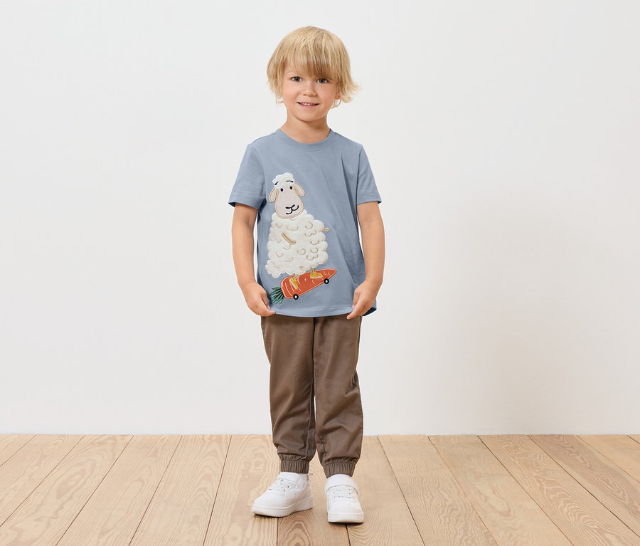 Junge trägt ein blaues T-Shirt mit einem Schaf auf einem Karotten-Skateboard.