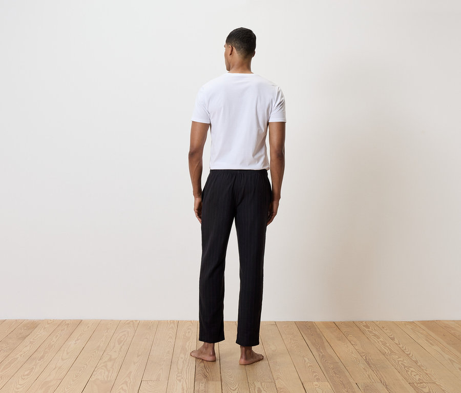 Ein Mann steht mit dem Rücken zur Kamera und trägt ein weißes T-Shirt und eine schwarze, gestreifte Hose.