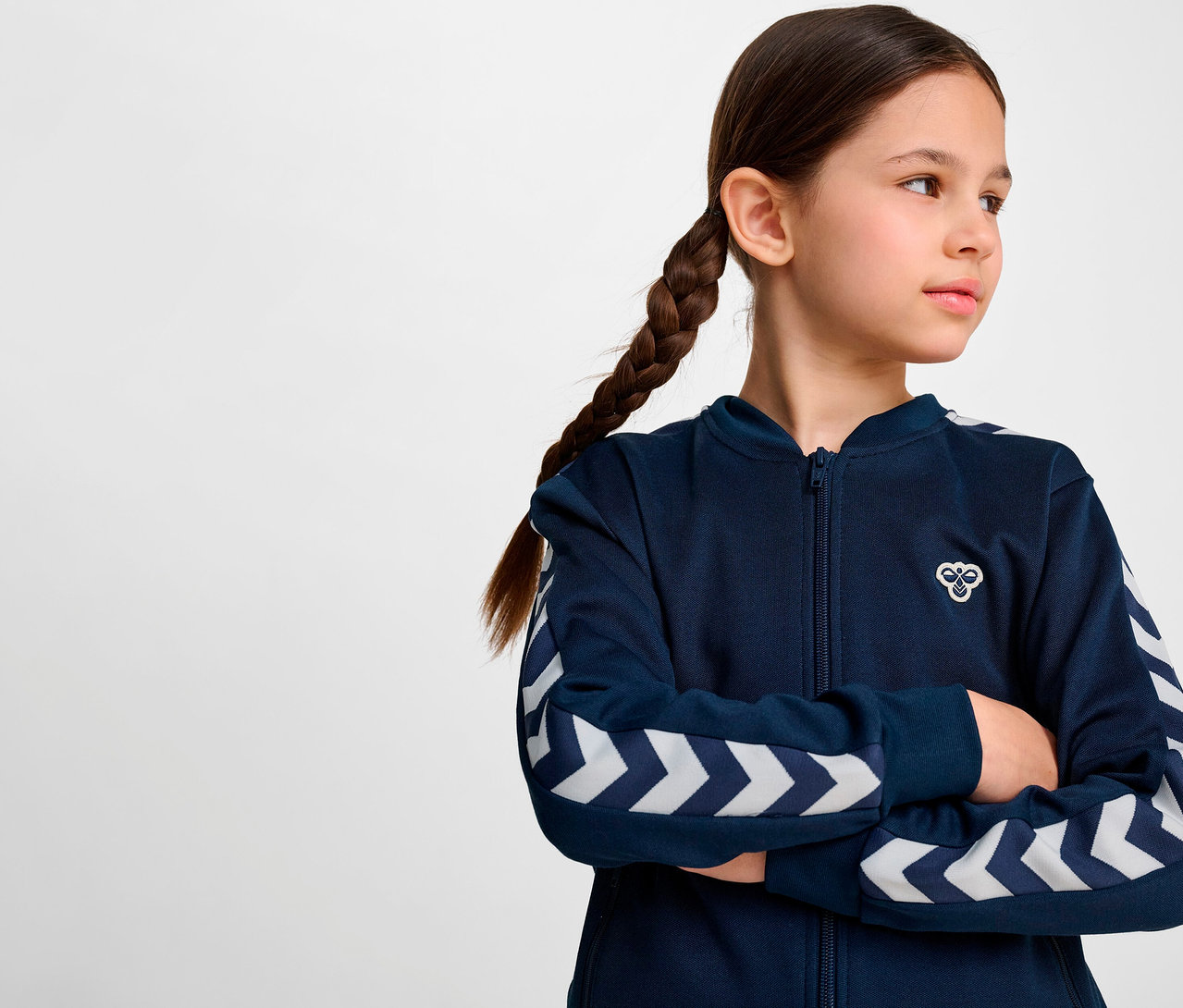 Mädchen mit Zopf trägt blaue HUMMEL HMLJR Archive Reg Poly Zip Jacket.