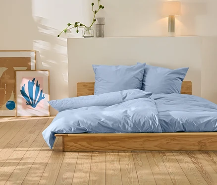 Ein Bett mit blauer Bettwäsche steht auf einem Holzboden. Hinter dem Bett befinden sich zwei Bilder.