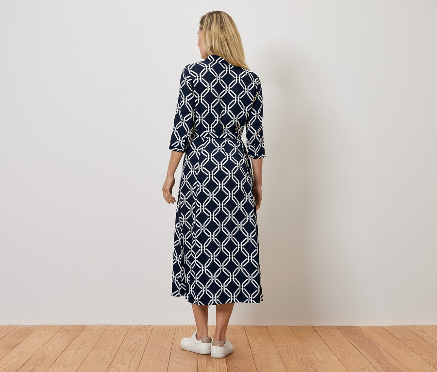 Rückansicht einer Frau in einem marineblauen Kleid mit weißem geometrischem Muster und weißen Turnschuhen.
